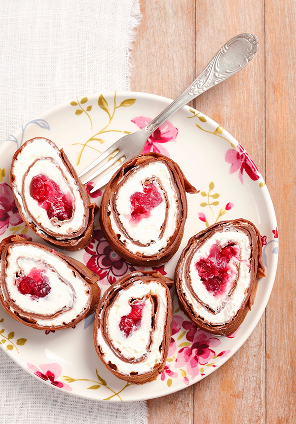 Schokoladen-Pfannkuchen auf einem Teller, garniert mit frischen Früchten und Puderzucker.